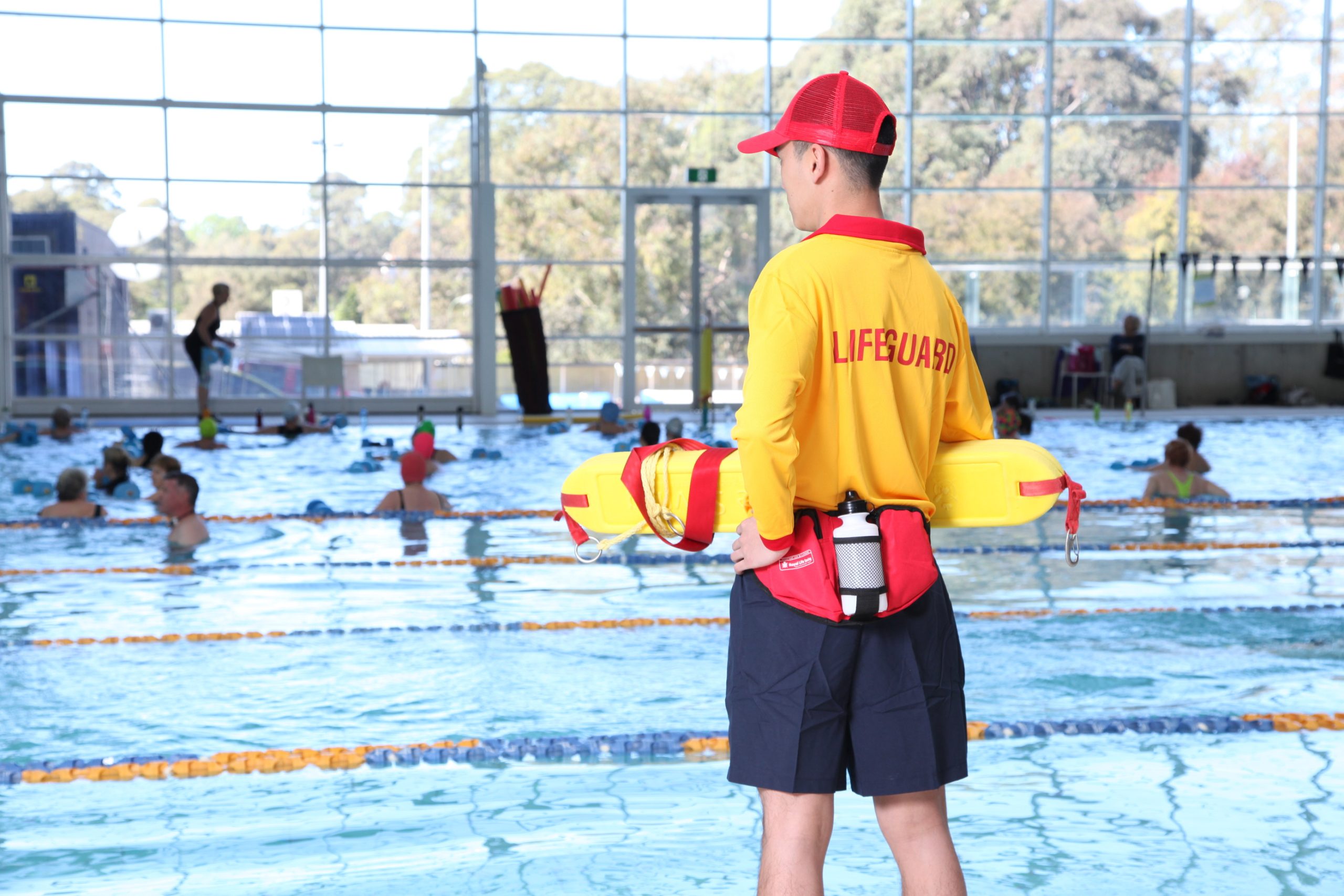 Lifeguard standing beside an indoor swimming pool.